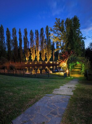 Un chemin de pierres menant à un bâtiment entouré d’une clôture et bordé d’arbres.