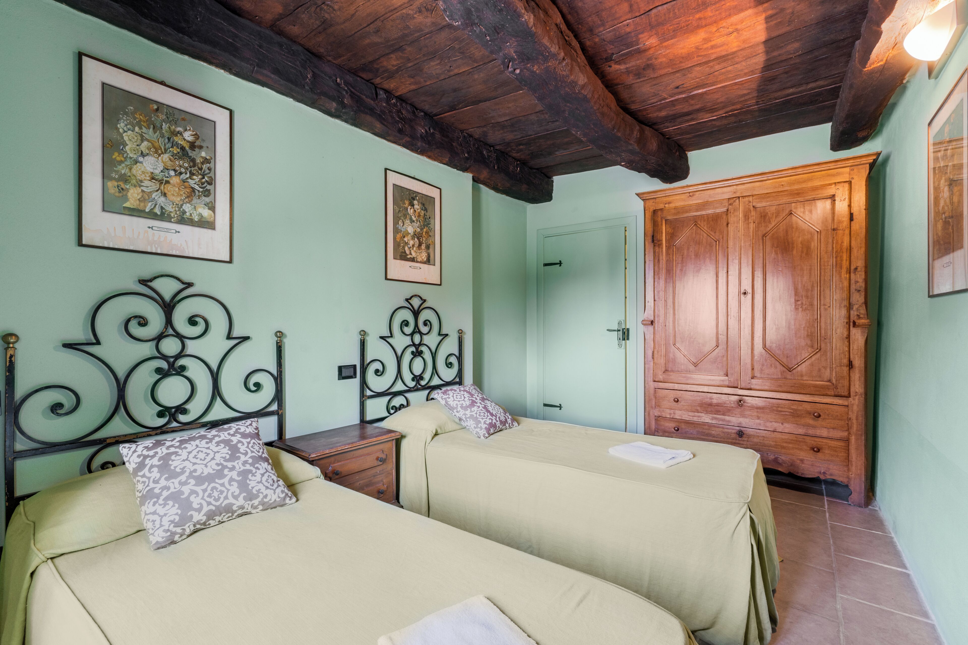 A room with two beds, wooden wardrobe, and framed pictures on the wall.