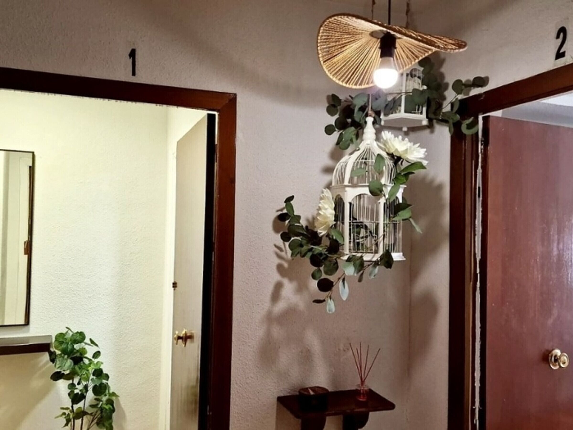 Een kamer met een houten deur, een witte muur, een hanglamp en een klein tafeltje met een kaars en wierookstokjes.