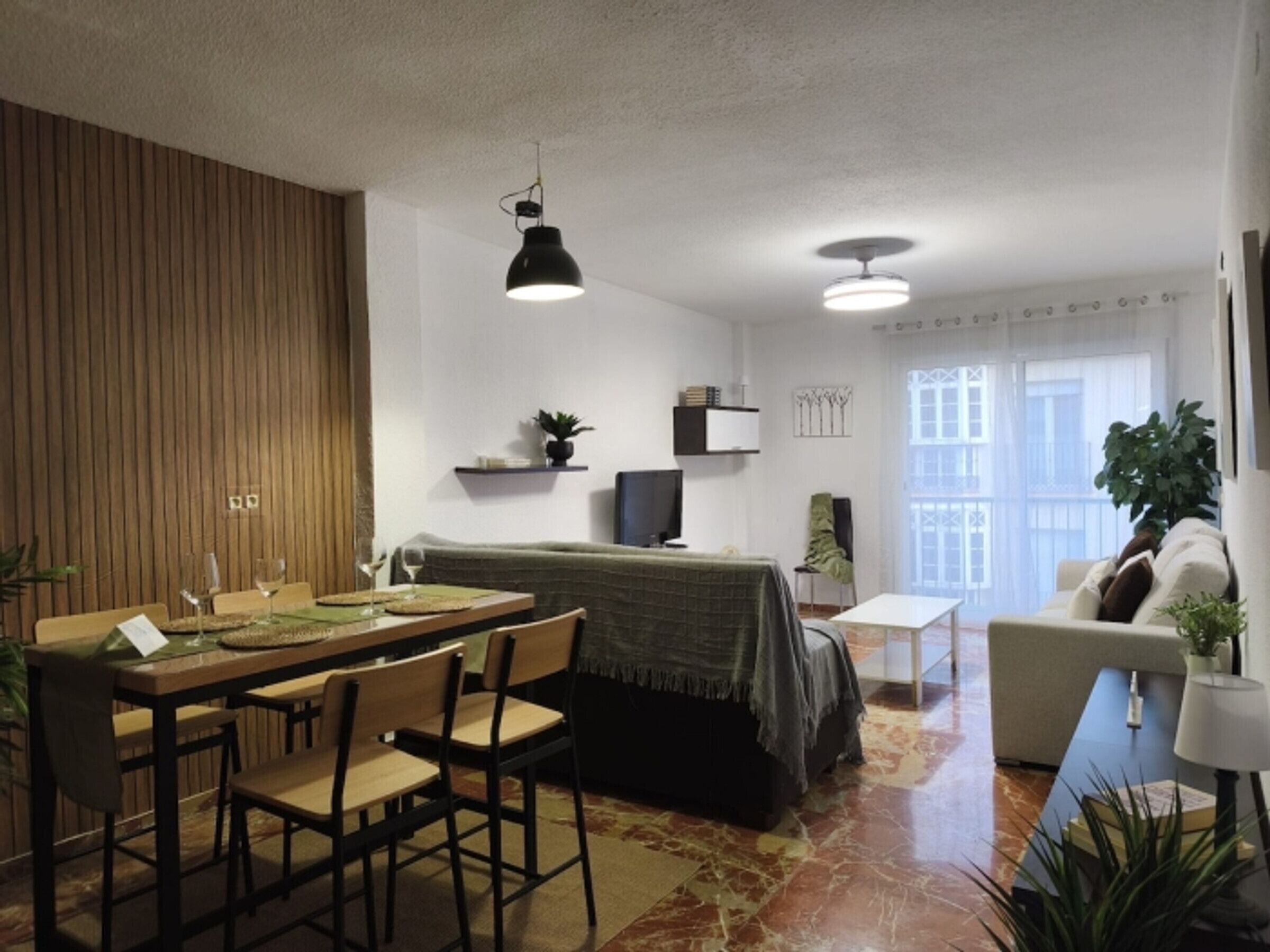 Een moderne woonkamer met een eethoek, een bank, een televisie en een balkon met uitzicht.