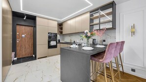 A modern kitchen with a marble countertop, a built-in oven, and a bar area with a vase of flowers. - Rondo ONZ Apt - 11th Floor, Air Con - by Rentujemy (Warszawa)
