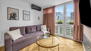 A modern living room with a sofa, a glass coffee table, and a large window with curtains. - Rondo ONZ Apt - 11th Floor, Air Con - by Rentujemy (Warszawa)