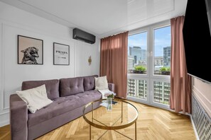 Ein modernes Wohnzimmer mit einer Couch, einem Glastisch und einem großen Fenster mit Vorhängen.