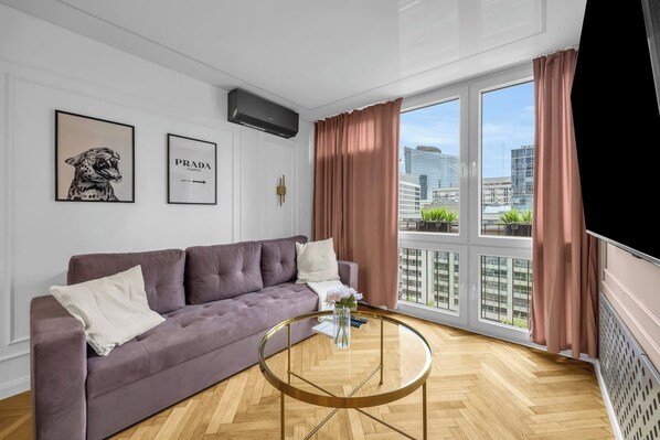 A modern living room with a sofa, a glass coffee table, and a large window with curtains. - Rondo ONZ Apt - 11th Floor, Air Con - by Rentujemy (Warszawa)