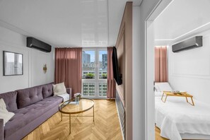 A modern hotel room with a sofa, a coffee table, a TV, a balcony with curtains, and a bed with a tray table. - Rondo ONZ Apt - 11th Floor, Air Con - by Rentujemy (Warszawa)