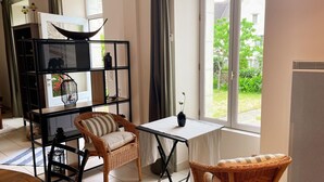 Ein Zimmer mit großem Fenster, Korbsesseln, einem kleinen Tisch und einer schwarzen Regaleinheit mit Dekorationsgegenständen.