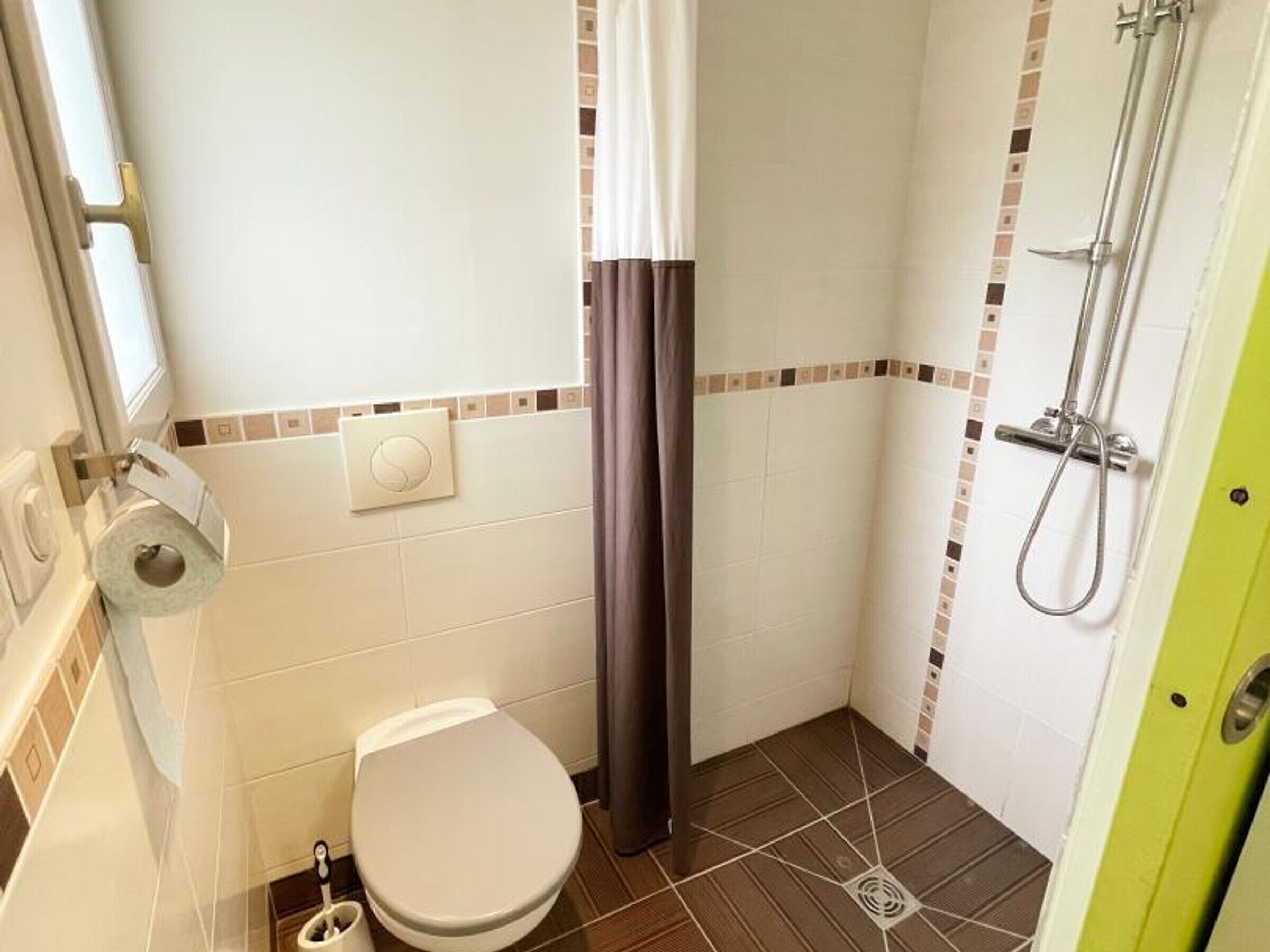 A small bathroom with a toilet, shower, and a toilet paper holder.