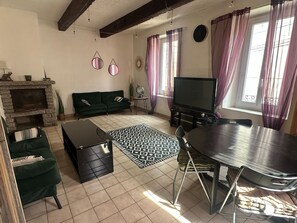 Ein Wohnzimmer mit Kamin, Sofa in Grün, Fernseher, Esstisch und einem gemusterten Teppich.