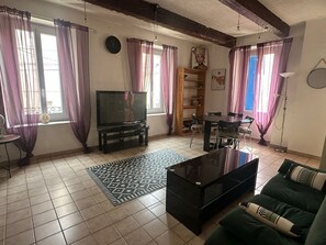 Ein Wohnzimmer mit Fernseher, Esstisch, Stühlen, einer Couch und einem gemusterten Teppich.