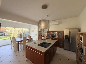 A modern kitchen with a central island, stainless steel appliances, and a dining area with chairs.