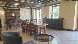 A dining area with a wooden table and chairs, a chessboard on a small table, and a stone wall with a decorative pattern. - Cottage by the water - 8 guests (Chérancé)