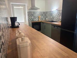 Eine Küche mit Holztischplatte, einer schwarzen Kaffeemaschine, einem Geschirrspüler und einem Kühlschrank.