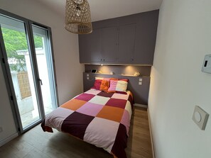 Ein Schlafzimmer mit Bett, Nachttisch, Lampe, Fenster und Tür.