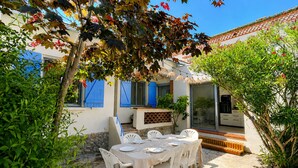 An outdoor patio with a table set for dining, surrounded by greenery and a building with blue shutters. - Air-conditioned house near beach - 6 guests (Argelès-sur-Mer)