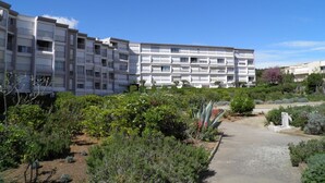 Ein mehrgeschossiges Wohngebäude mit Balkonen, umgeben von gepflegten Gärten und blauem Himmel.