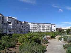 A multi-story residential building with balconies, surrounded by landscaped gardens and a clear sky. - Studio cabin beachfront, parking - 2 guests (Sète)