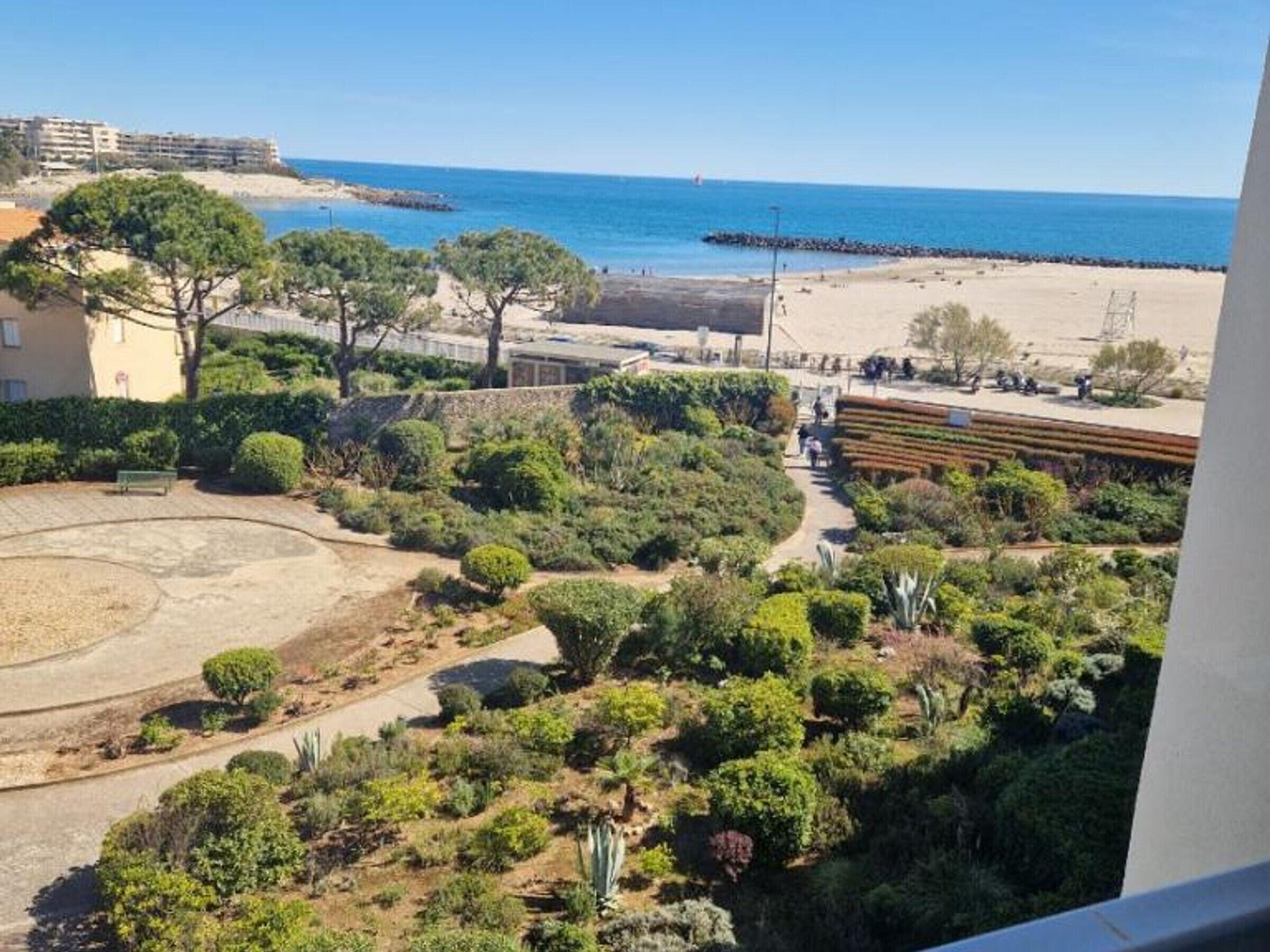 A landscaped garden with a circular area, a pathway, and a view of the beach and ocean.