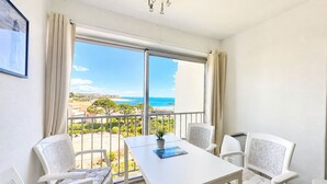 Ein Balkon mit einem weißen Tisch und Stühlen, einem Topf mit einer Pflanze und Blick auf Strand und Meer.