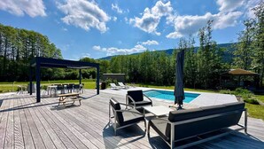 Una terraza de madera con mobiliario exterior, una piscina y un pabellón.