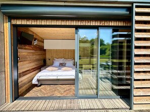 Ein modernes Schlafzimmer mit einer Wand aus Holzlamellen, einem Bett mit weißer Bettwäsche und einer Glastür zum Außenbereich.
