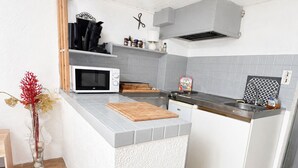 Een kleine keuken met een magnetron, een klein fornuis, een snijplank en een spoelbak.