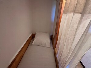 Ein kleiner, schmaler Raum mit einem Einzelbett, einem Holzkopfstück und einem transparenten Vorhang.