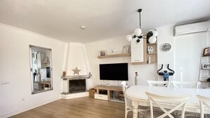 Een woonkamer met een open haard, een flatscreen-tv, een eettafel met stoelen en een plafondlamp.
