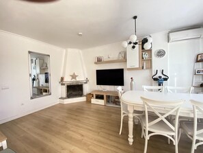 A living room with a fireplace, a flat-screen TV, a dining table with chairs, and a ceiling light fixture. - Spacious townhouse - 6 guests (Salou)
