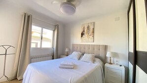Een hotelkamer met een groot bed, een nachtkastje met een lamp, een radiator en een raam met gordijnen.