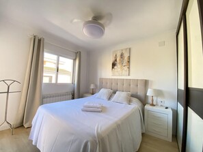 A hotel room with a large bed, a bedside table with a lamp, a radiator, and a window with curtains. - Spacious townhouse - 6 guests (Salou)