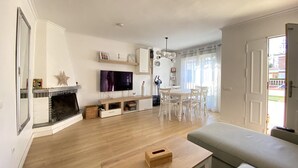 Een woonkamer met een open haard, televisie, eettafel en een bank.
