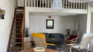 Avoin, loft-tyylinen huone, jossa on puinen pöytä, tuoleja, sohva, tikkaat ja riippuvalaisin.