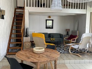 A loft-style room with a wooden table, chairs, a sofa, a ladder, and a hanging light fixture. - Family house 150m from the beach - 7 guests (Capbreton)