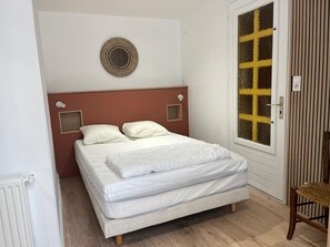 A bedroom with a bed, a round wall vent, a window with yellow grid, and a wooden chair. - Family house 150m from the beach - 7 guests (Capbreton)
