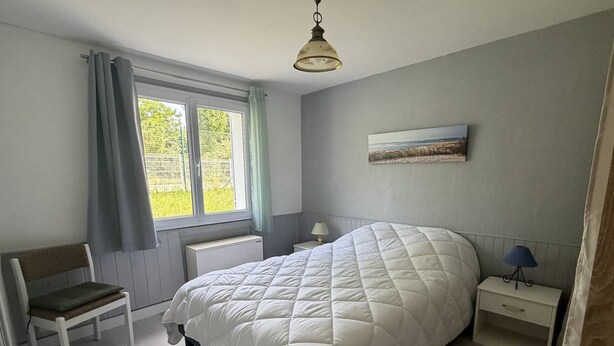 Ein Schlafzimmer mit einem großen Bett, einem Sessel, einem Nachttisch mit Lampe und einem Fenster mit Vorhängen.