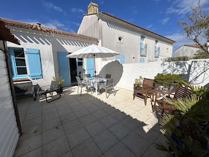 Un patio con tavolo e sedie, un ombrellone bianco e una porta blu.