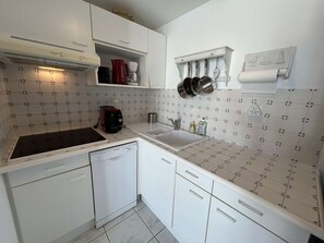 Una cocina compacta con armarios blancos, lavavajillas integrado, estufa y pileta.