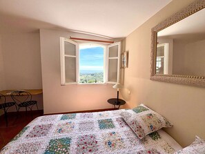 Ein Schlafzimmer mit Bett, Fenster mit Blick, Schreibtisch und Stuhl.
