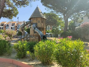 A playground with a slide and climbing structures, surrounded by greenery and residential buildings. - Air-conditioned apartment - relaxing setting (Le Barcarès)