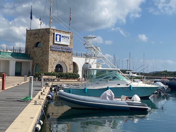 A marina with boats docked, a stone building with a sign for MOYS Marina di Olbia Yacht Services, and a wooden dock. - MOYS APARTMENT SEA VIEW OLBIA (Olbia)