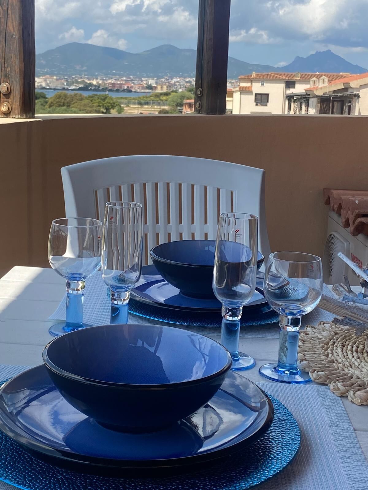 A table set with blue dinnerware and wine glasses, overlooking a cityscape with mountains in the distance.