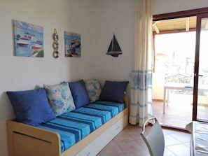 A small room with a sofa bed, a table, and a chair. There are three paintings on the wall. - MOYS APARTMENT SEA VIEW OLBIA (Olbia)