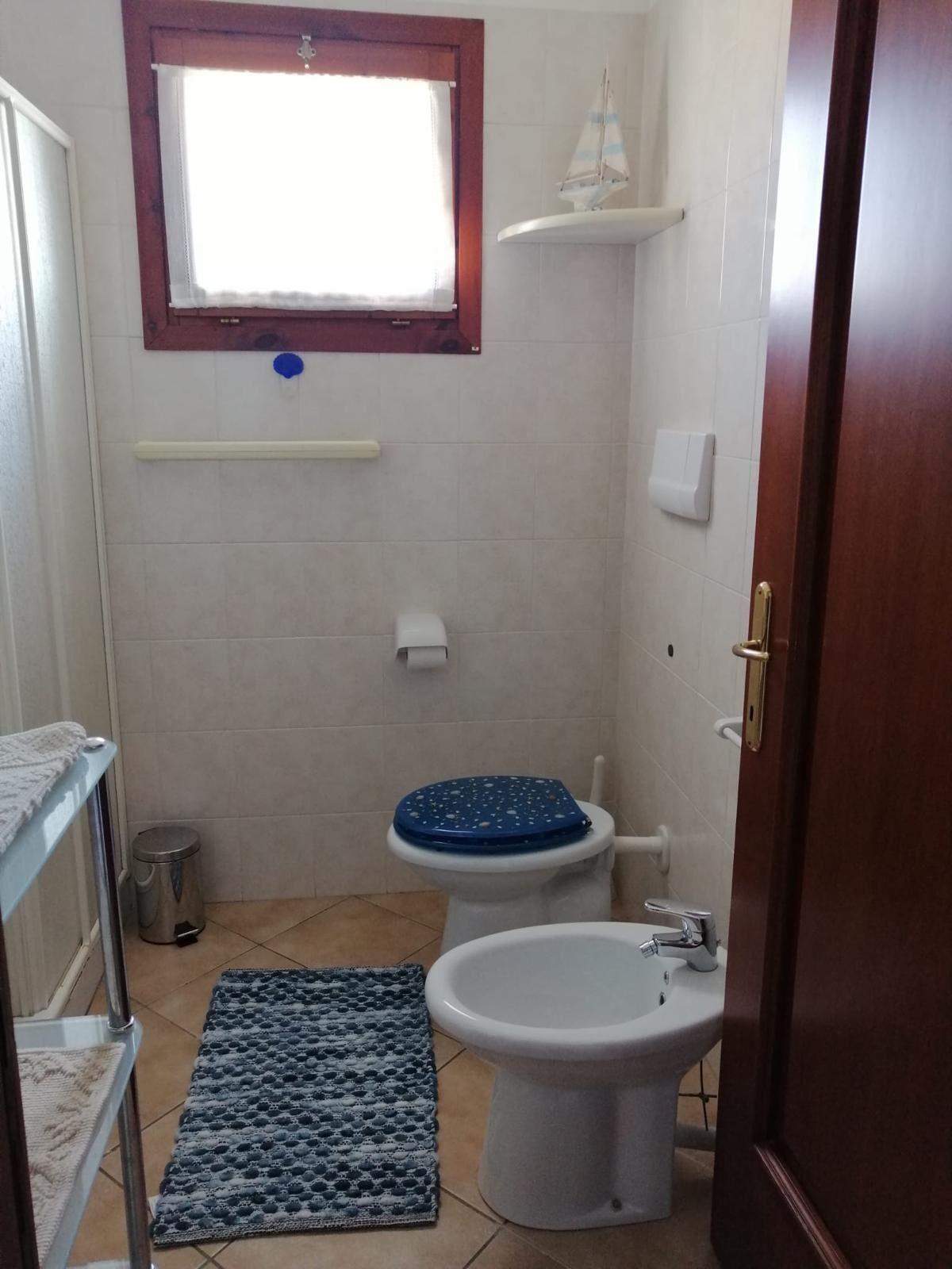 Een kleine badkamer met toilet, bidet en een raam boven de wastafel.