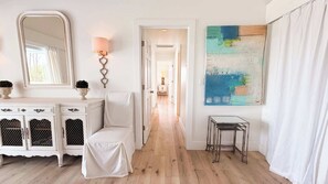 A hallway with a white chair, a white console table with decorative items, a wall-mounted lamp, and a metal table. - Quiet Family Home | Close to Beach, Restaurants, Boating | Daily Activity Deals (Orange Beach)