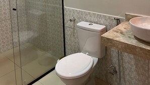 Casa de banho com sanita, lavatório, chuveiro e espelho.