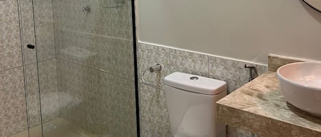 A bathroom with a toilet, a sink, a shower, and a mirror.