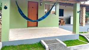 Uma casa com fachada verde, porta de madeira, rede e um espaço de varanda.