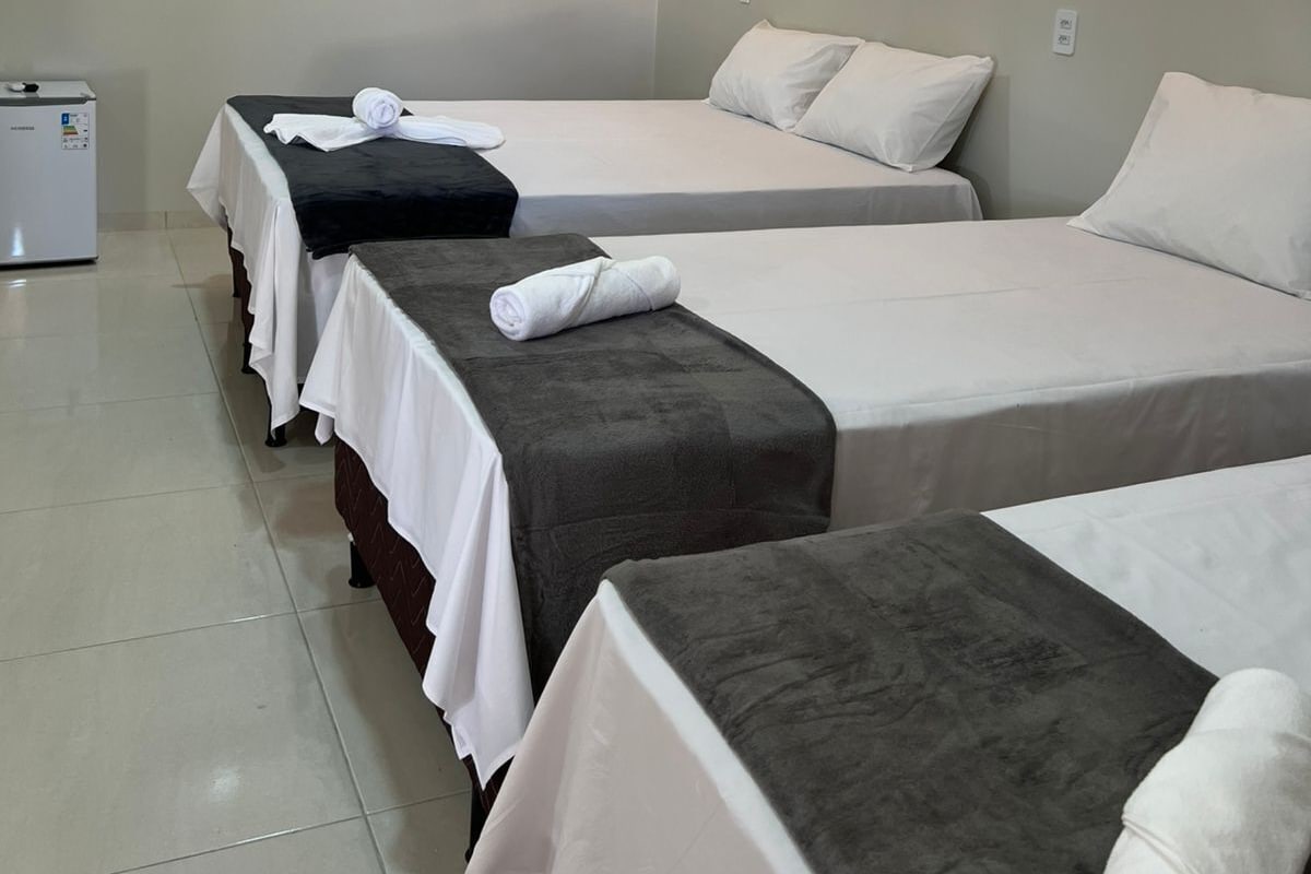 A hotel room with three beds, a white air conditioner, and two hanging pendant lights.