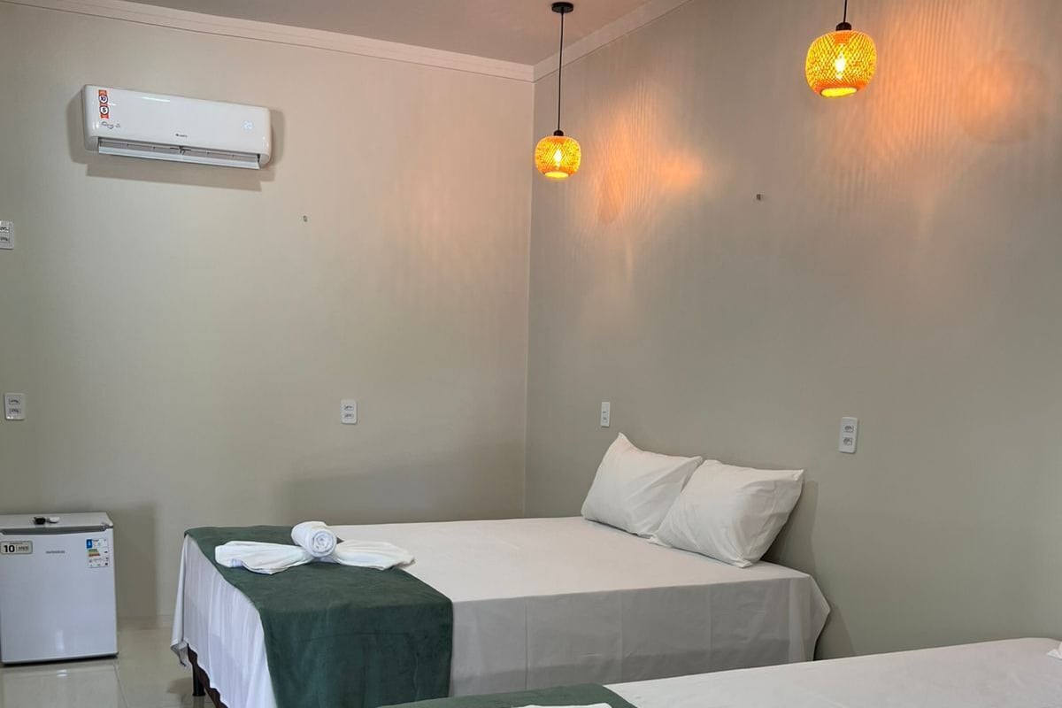 A hotel room with two beds, a refrigerator, and an air conditioning unit.