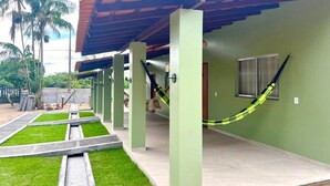 Um espaço coberto ao ar livre, com piso de concreto, paredes verdes e uma rede.